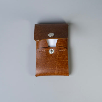 A detailed edge view of a tan brown leather card holder with a snap button closure, shown against a plain light gray background.