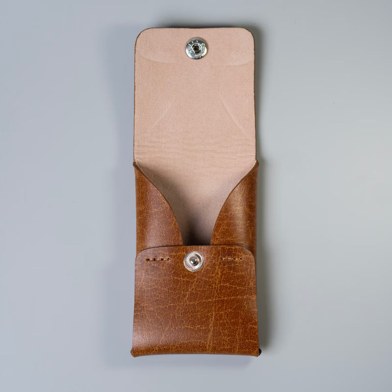 A tan brown leather card pouch with a beige interior felt lining, featuring a flap with a snap-button closure made by 'The Bicyclist', shown against a neutral gray background.