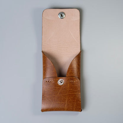 A tan brown leather card pouch with a beige interior felt lining, featuring a flap with a snap-button closure made by 'The Bicyclist', shown against a neutral gray background.