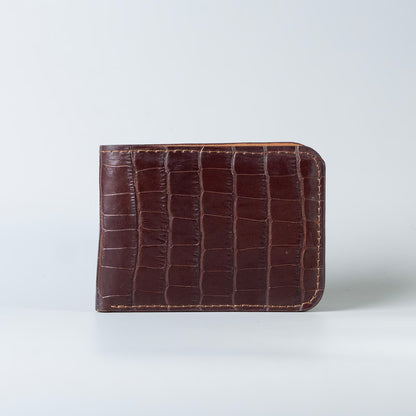A maroon full grain leather bifold wallet with an embossed crocodile pattern, from The Bicyclist shown standing upright on a light gray background.