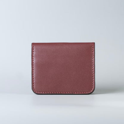 A slim compact maroon full grain leather card holder wallet with visible stitching from The Bicyclist, photographed upright against a light gray studio background.