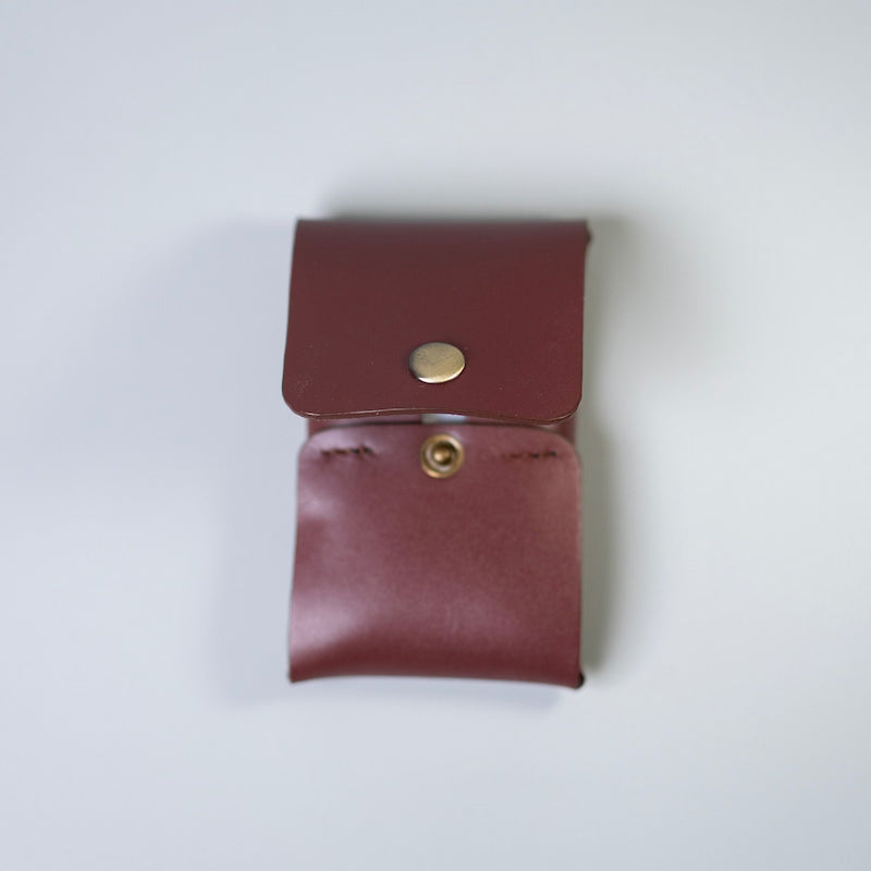 A small maroon or burgundy leather pouch with a snap-button closure, photographed from above on a light gray background.