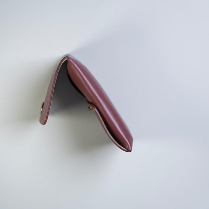 A small full grain leather card pouch or card case in a maroon color, made by 'The Bicyclist' shown from an overhead angle on a clean white background.