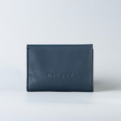 A dark navy blue full grain leather card holder wallet with debossed branding of 'The Bicyclist' on the back, photographed against a clean, light gray studio background.