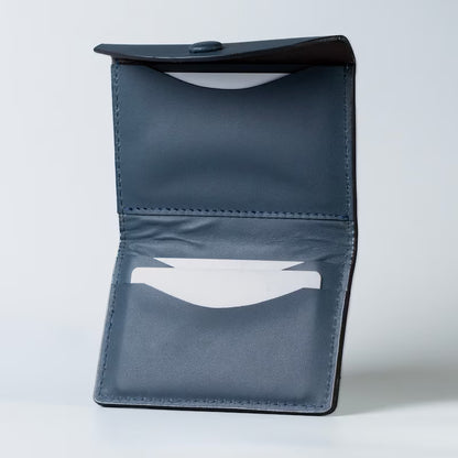 A dark blue full grain leather card holder wallet shown open, displaying its interior stitching, button closure, and card slots with white plastic cards inserted into the card slots against a light gray background.