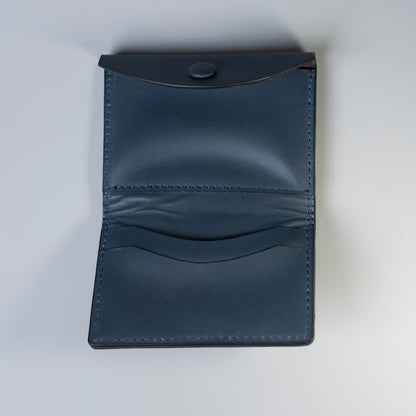 A dark navy blue full grain leather card holder wallet shown open, featuring a snap-button closure on the top flap and multiple card slots on the interior, photographed on a light gray background.