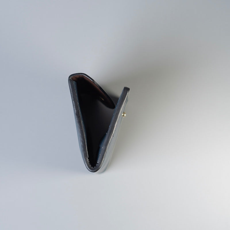 A handpainted side edge detail image of a navy blue full grain leather wallet shown open from a top-down angle, revealing a black interior and a small gold-tone metal snap button on the side, set against a light gray background.