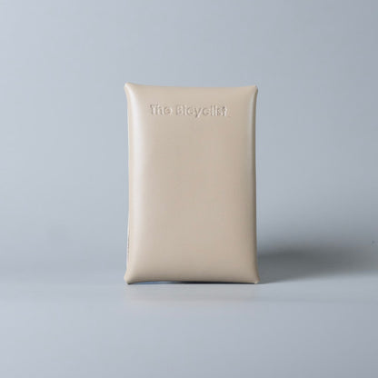 Back side of a off white full grain leather card case with the brand name 'The Bicyclist' embossed at the top, set against a solid light gray background.