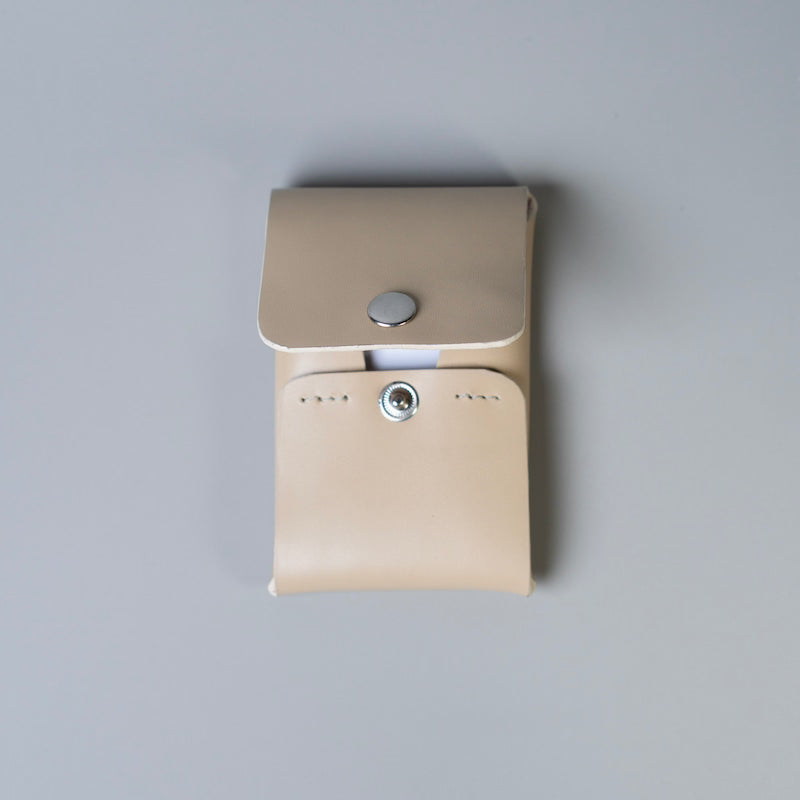 A off white full grain leather card holder with a snap button closure, shown from a top-down view on a neutral gray background.
