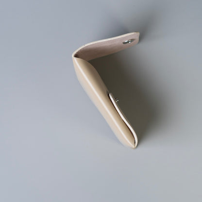 A minimalist, side view of a full grain leather card holder from The Bicyclist with a snap button closure shown from an overhead angle against a solid gray background.