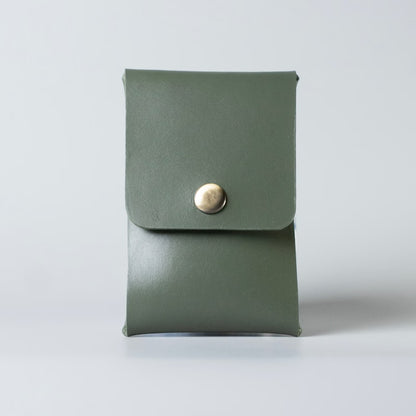 An olive green full grain leather business card case with a flap closure and a single gold-tone snap button, made by 'The Bicyclist' photographed against a neutral light gray background.