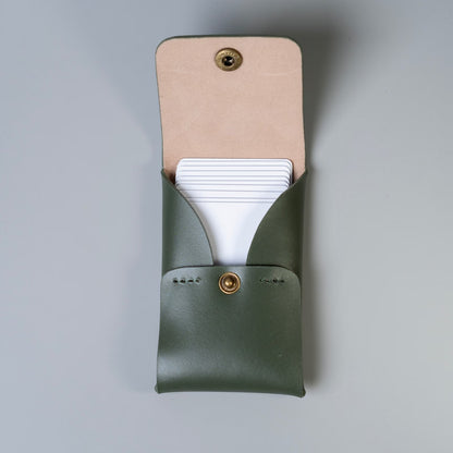 An olive green full grain leather business card holder with a beige felt lined flap and a gold snap button shown open, made by 'The Bicyclist' with white plastic cards partially tucked inside, set against a neutral gray background.