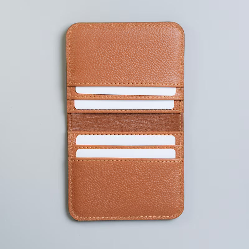 A tan pebbled leather card holder wallet with multiple card slots with white plastic cards inserted in them, shown open against a light gray background.