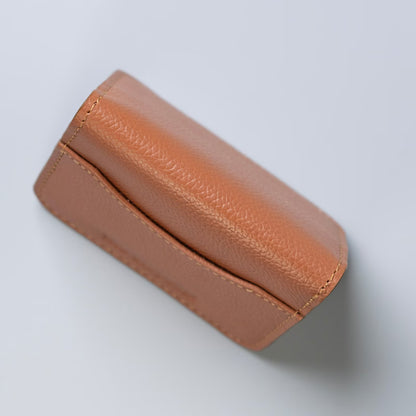 A tan pebbled leather pouch or case shown at an angle on a light gray background.