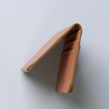A minimalist tan leather card holder wallet shown from an angled deatiled side view on a light gray background.