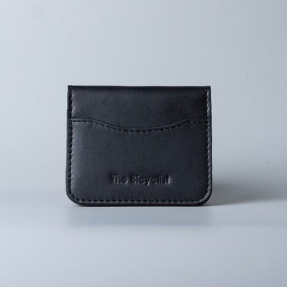 A black full grain leather card holder wallet with visible stitching and debossed 'The Bicyclist' logo, centered on a light gray background.