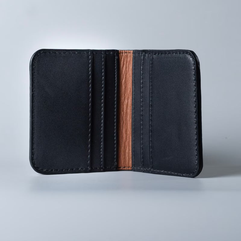 Open view of a black full grain leather bifold card wallet with 6 card slots and tan sheep leather lining inside on a soft grey background 