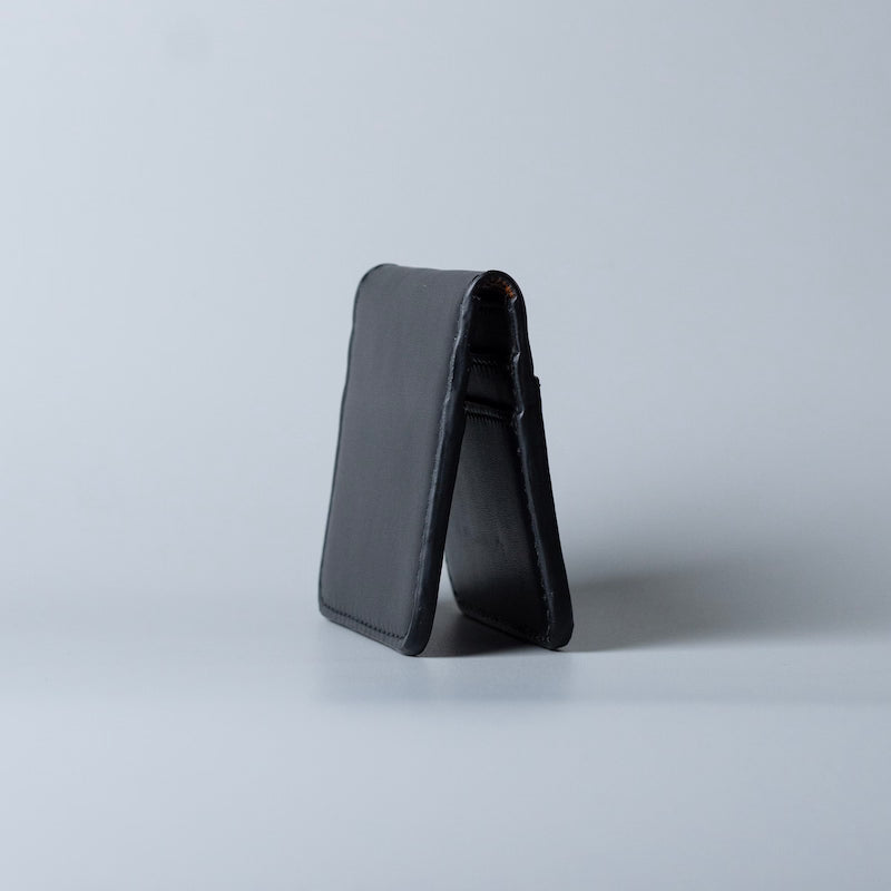 A black full grain leather card holder or wallet from 'The Bicyclist' standing open on a light gray studio background.
