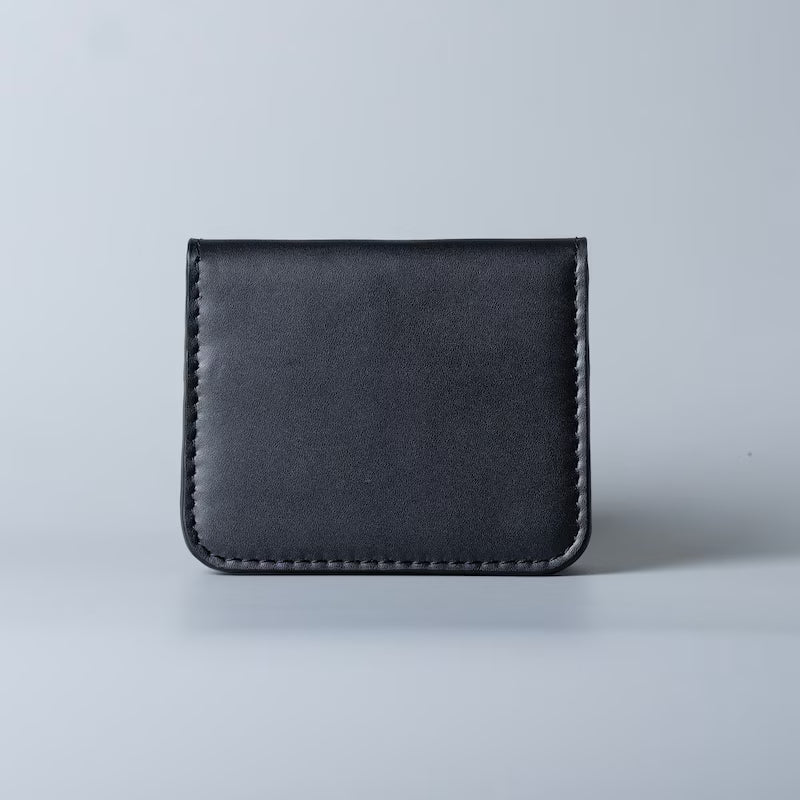 A minimalist black leather card holder or wallet with visible stitching along the edges, photographed against a clean light gray background.
