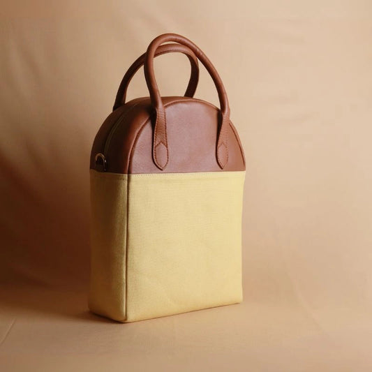 Perspective view of a yellow canvas and tan leather work handbag with a zip