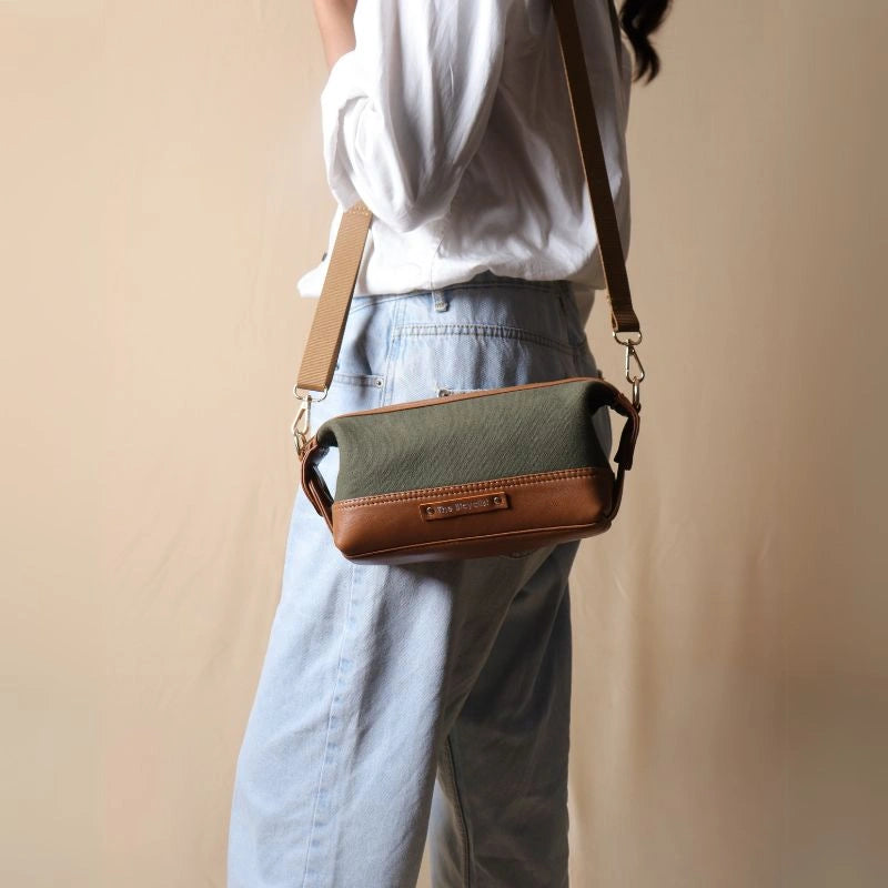 Woman in a white shirt carrying a dark green canvas and tan leather pouch as a side sling