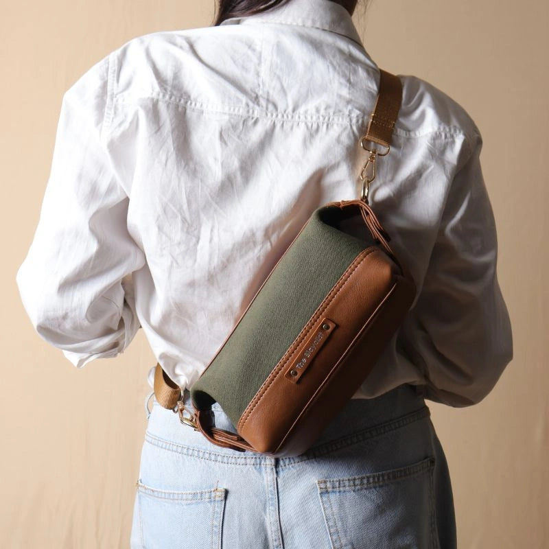 Woman in a white shirt carrying a dark green canvas and tan leather pouch dopp kit as a crossbody sling