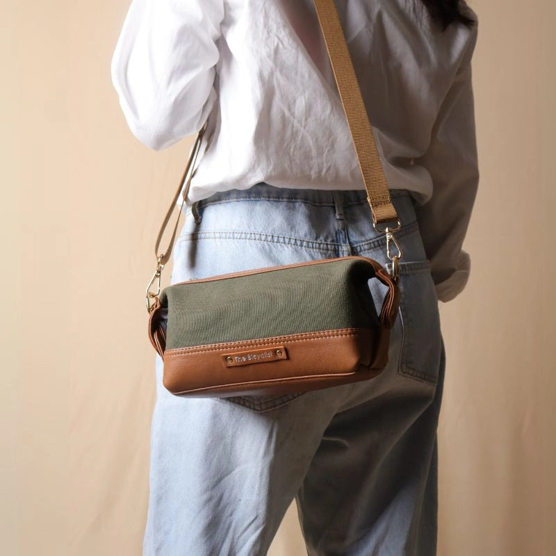 Woman in a white shirt carrying a dark green canvas and tan leather pouch as a side sling
