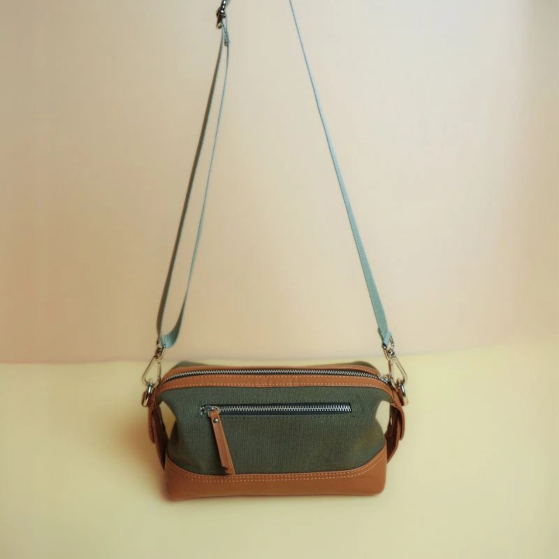 Front view of a dark green cotton canvas and tan leather dopp kit with zip and shoulder straps extended