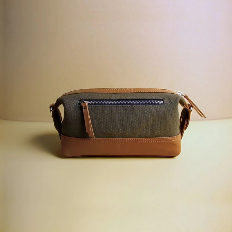 Front view of a dark green cotton canvas and tan leather dopp kit with zip