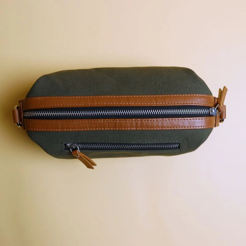 Top view of a dark green cotton canvas and tan leather dopp kit with a metal zip