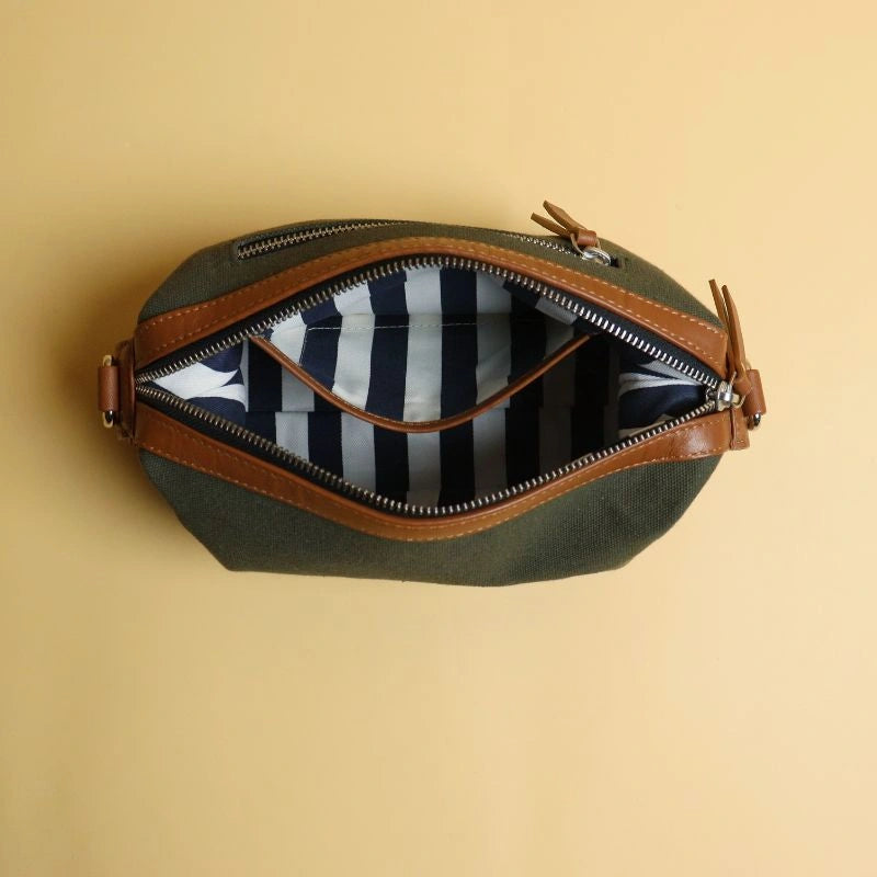 Top Open view of a dark green cotton canvas pouch and tan leather dopp kit with zip, stripe cotton lining and a open internal pocket.