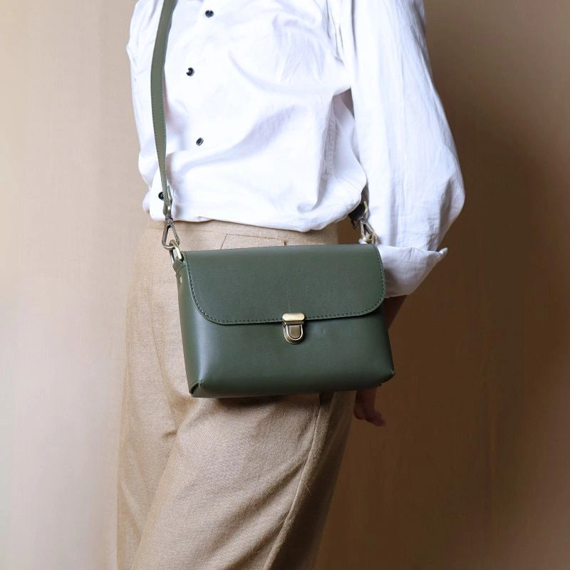 Woman in a white shirt carrying a green leather crossbody shoulder sling bag with a flap and a soft gold push lock over her shoulder 