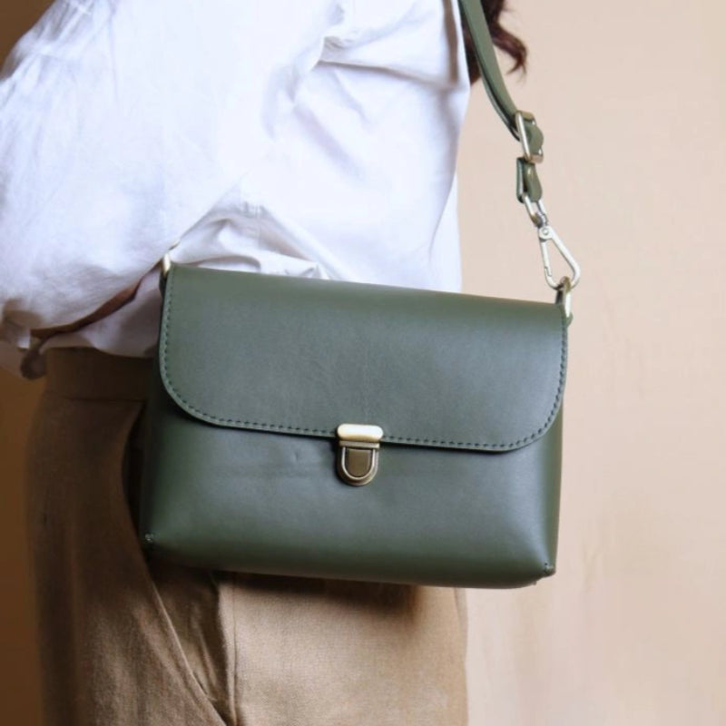 Woman in a white shirt carrying a green leather crossbody shoulder side bag with a flap over her shoulder