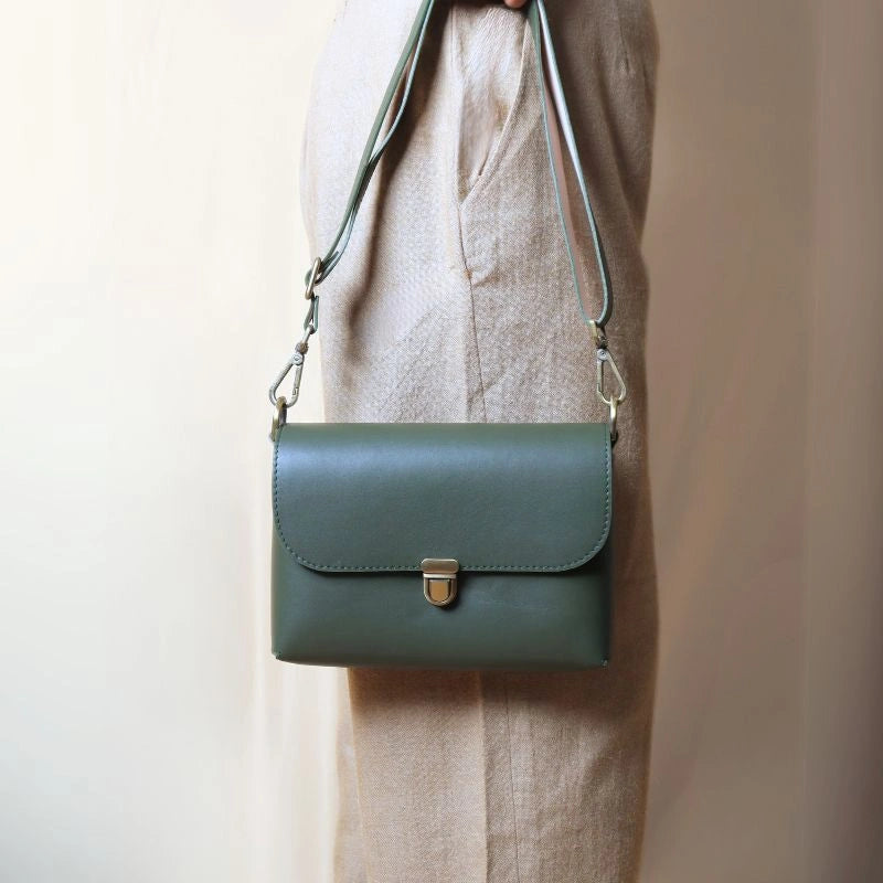 Woman in beige trousers holding a green crossbody shoulder sling bag with a flap and soft gold push button lock in her hand
