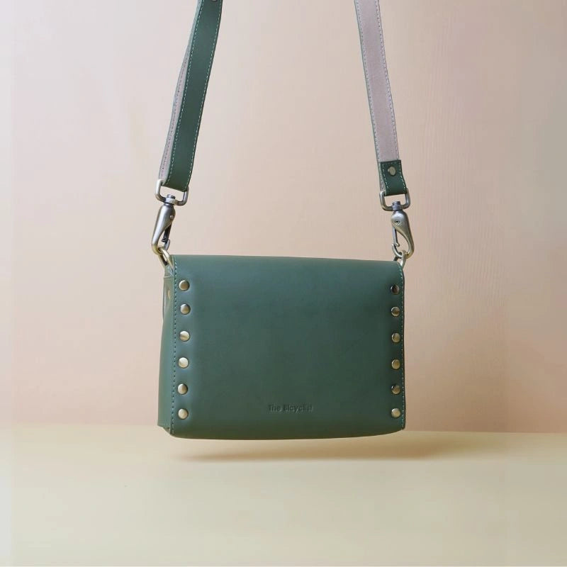 Back view of a green leather crossbody shoulder sling bag with soft got rivets and fittings