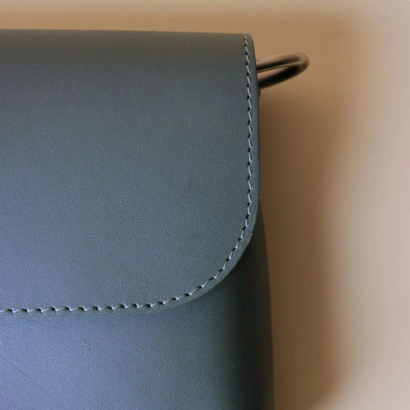Detailed stitching view of the flap of a green leather crossbody shoulder sling bag