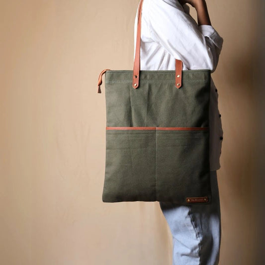 Woman in a white shirt and light blue denims carrying over her shoulder, a dark green canvas tote with leather straps and leather trim front pocket