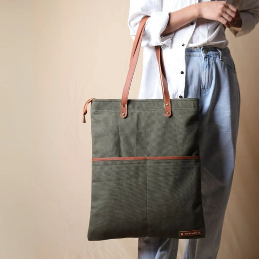 Woman in a white shirt and light blue denims carrying on her hand, a dark green canvas tote with leather straps and leather trim front pocket