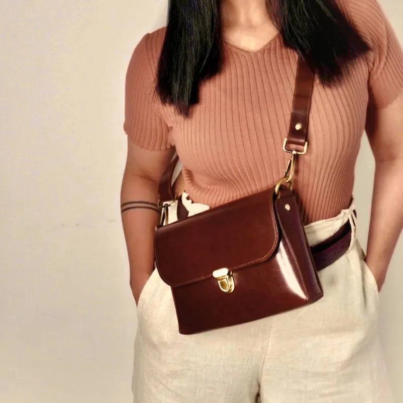 Dark Brown Leather Crossbody Sling Bag with a Flap and Light Gold Pushlock and fittings on a model with black hair and a peach top on a white background