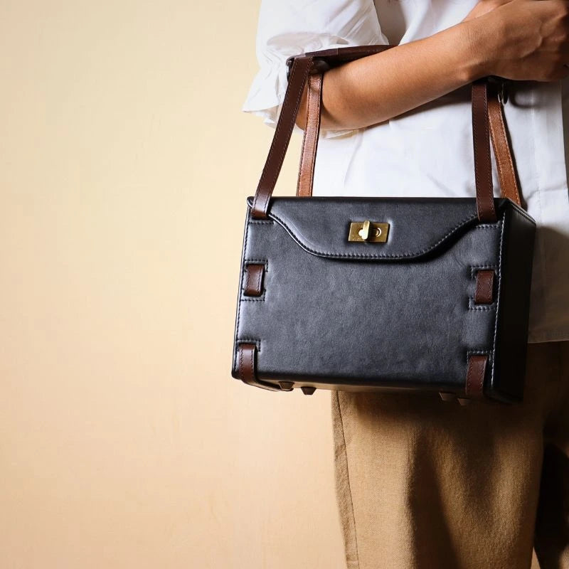 Structured Box Black Leather Shoulder Handbag with Dark Brown straps carried by a woman in her hand wearing a white shirt