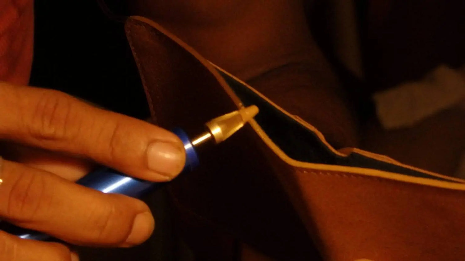 Zoomed in view of a leather craftsman putting the finishing touches on the edge of a leather wallet.
