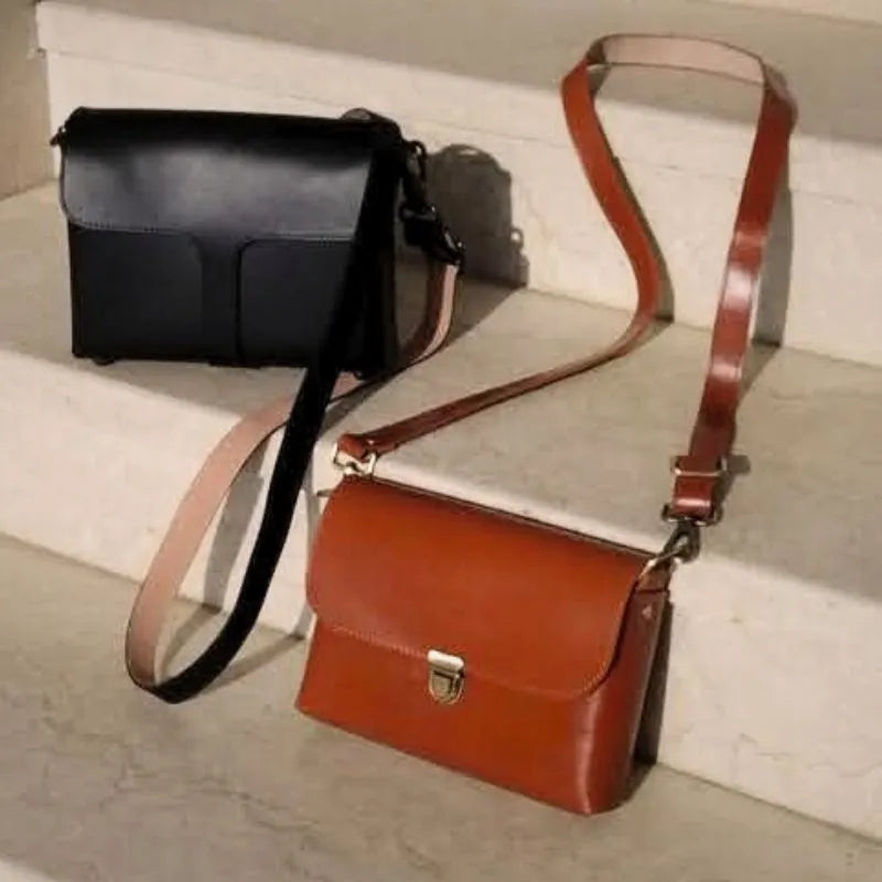 Black Leather Crossbody Sling Bag and a Tan Leather Crossbody Sling bag with a Push lock on a white marble staircase