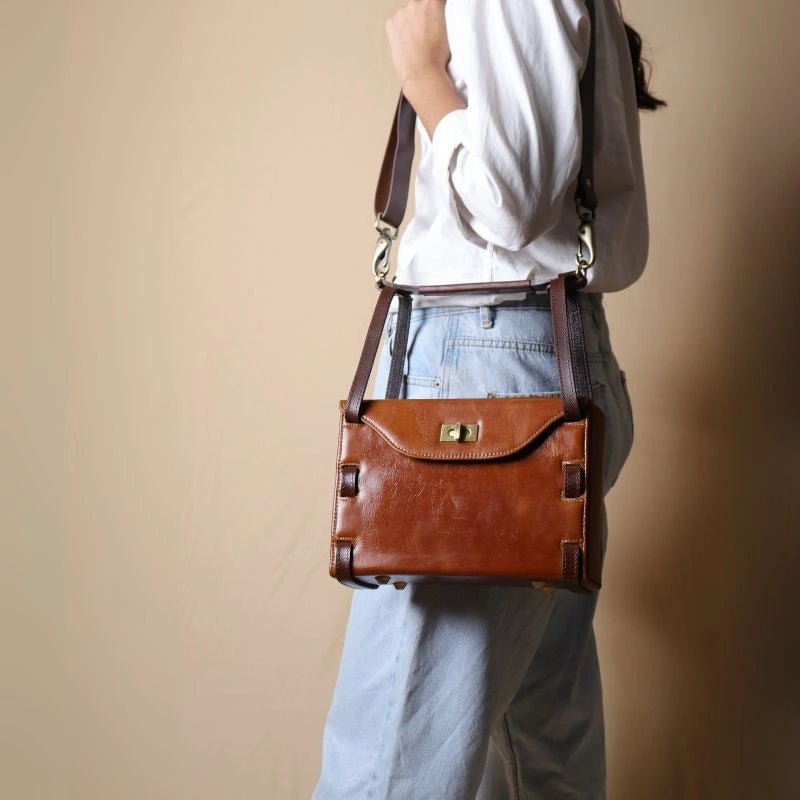 Woman in a White shirt carrying a structured box leather sling bag in tan with dark brown straps over her shoulder