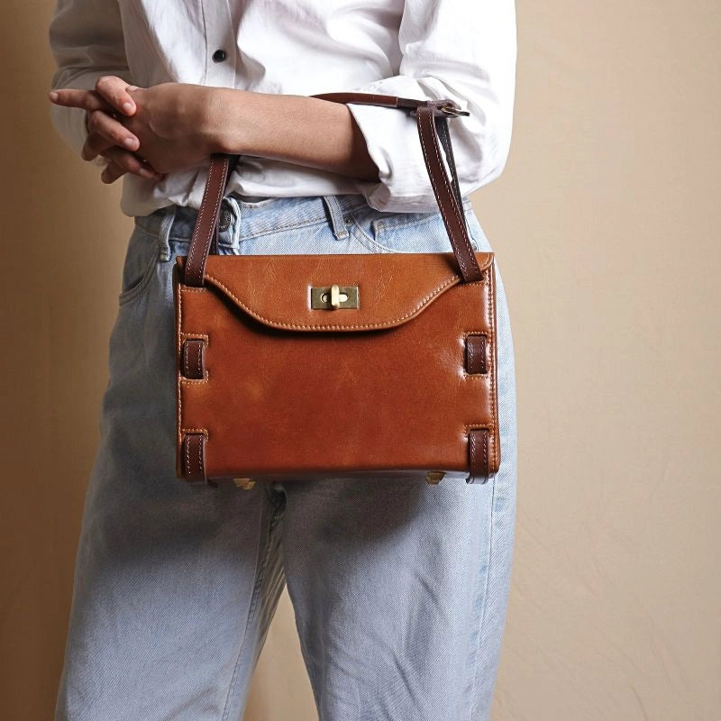 Woman in a White shirt carrying a structured box leather hand bag in tan with dark brown straps in her hand
