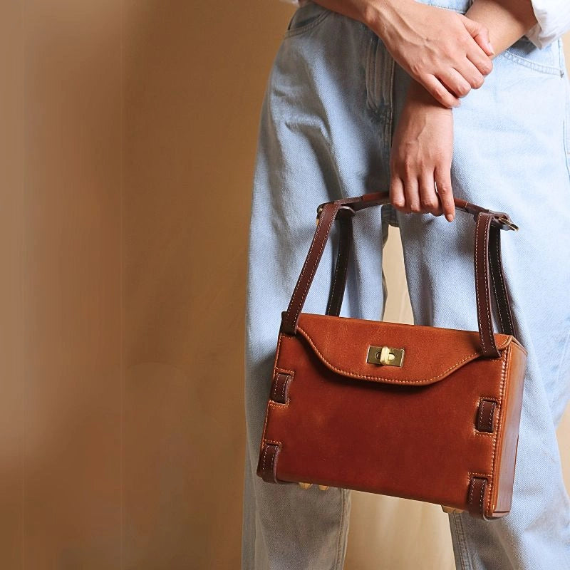Woman in light blue denims carrying a structured crossbody box leather sling hand bag in tan with dark brown straps in her hand