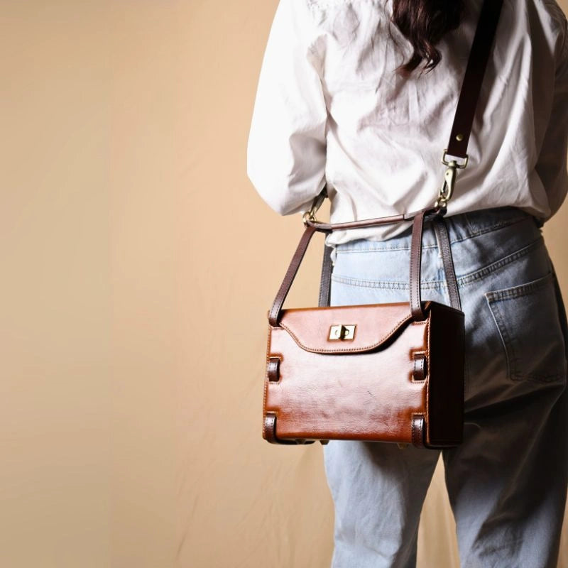 Back View of a Woman in a White shirt carrying a structured box leather sling bag in tan with dark brown straps over her shoulder
