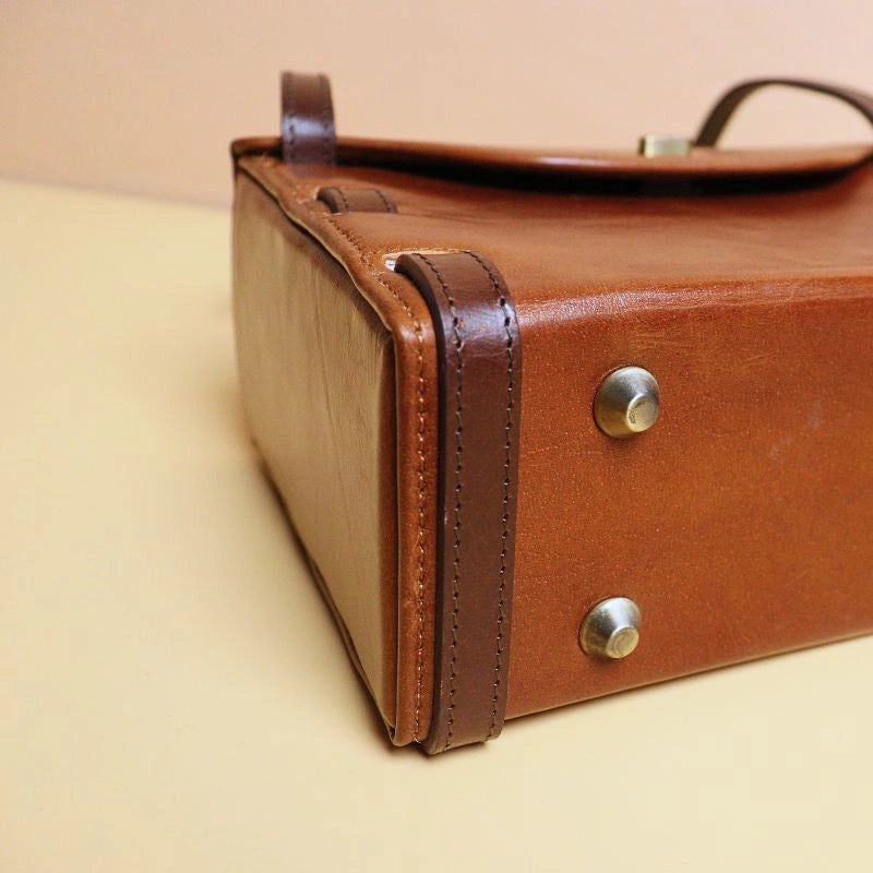 Detail Bottom View of a Tan Leather structured box crossbody handbag with dark brown straps with Golden base studs