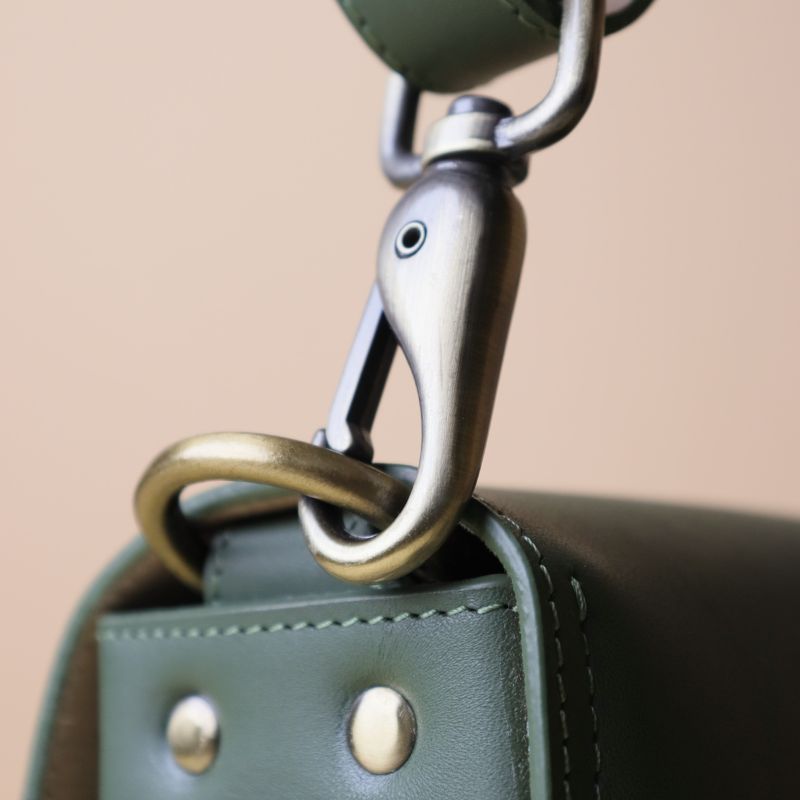 Olive green handmade leather women's crossbody structured sling bag with brass finished metal fittings and adjustable strap brass finished metal fitting detail view