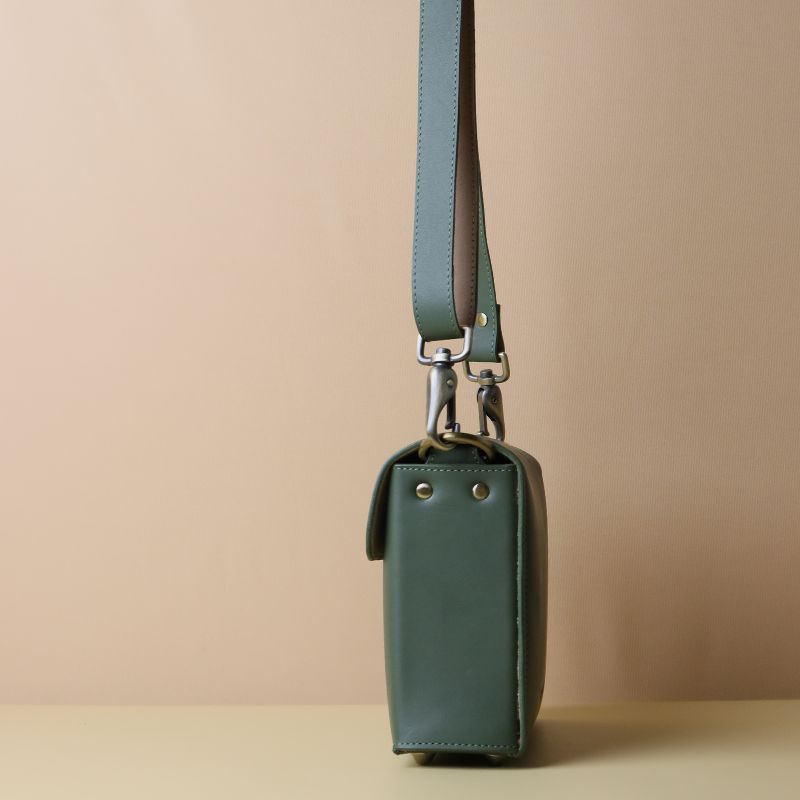Olive green handmade leather women's crossbody structured sling bag with brass finished metal fittings and adjustable strap side view