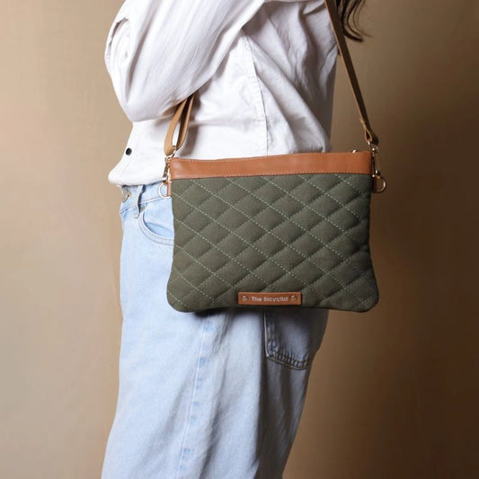 Woman in white shirt and blue denim carrying a quilted dark green canvas sling side bag with tan leather trims